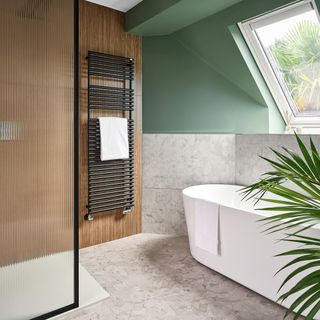 a bathroom with a bathtub, a reeded shower screen, green walls, and a black towel rail