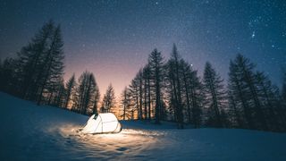 tent lit up on snow and below star filled sky