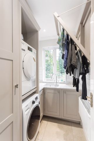 cream and white utility room with fold down clothes rack designed by Burlanes, and a washing machine and tumble dryer