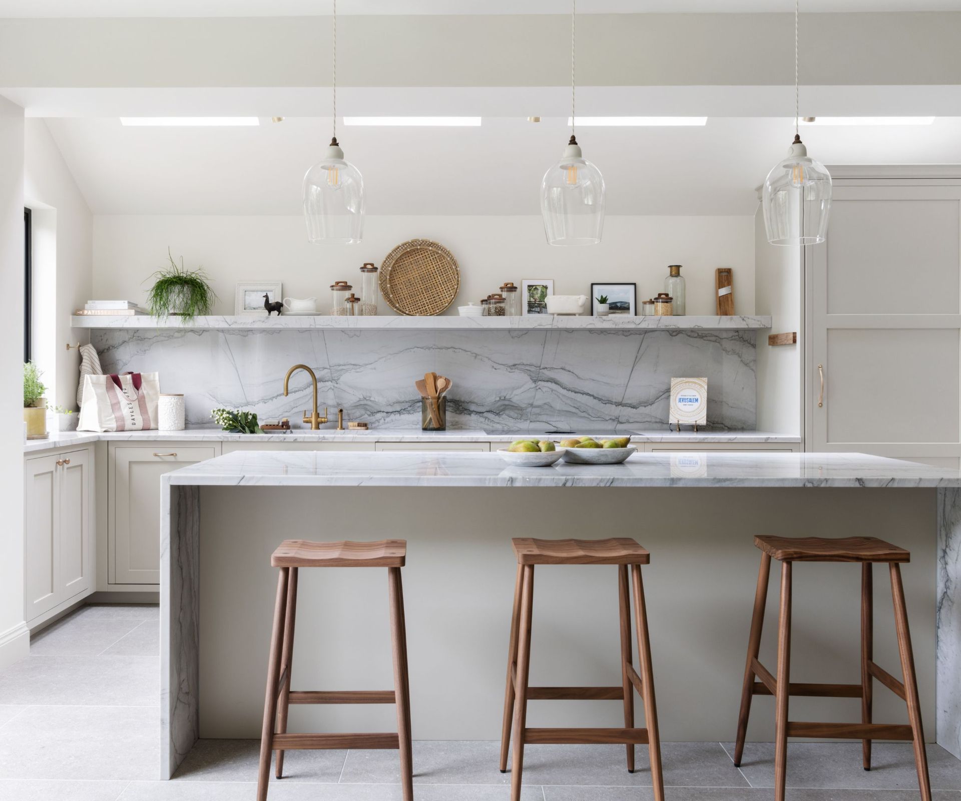 A kitchen with white cabinets and marble countertops, and open shelving filled with layered decor