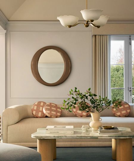 Contemporary living room lifestyle with sleek cream sofa, round mirror, marble and wooden coffee table, checkered round scatter cushions