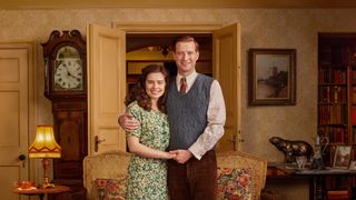 Rachel Shenton in a floral dress as Helen stands next to Nicholas Ralph in a jumper and trousers as James in All Creatures Great and Small.