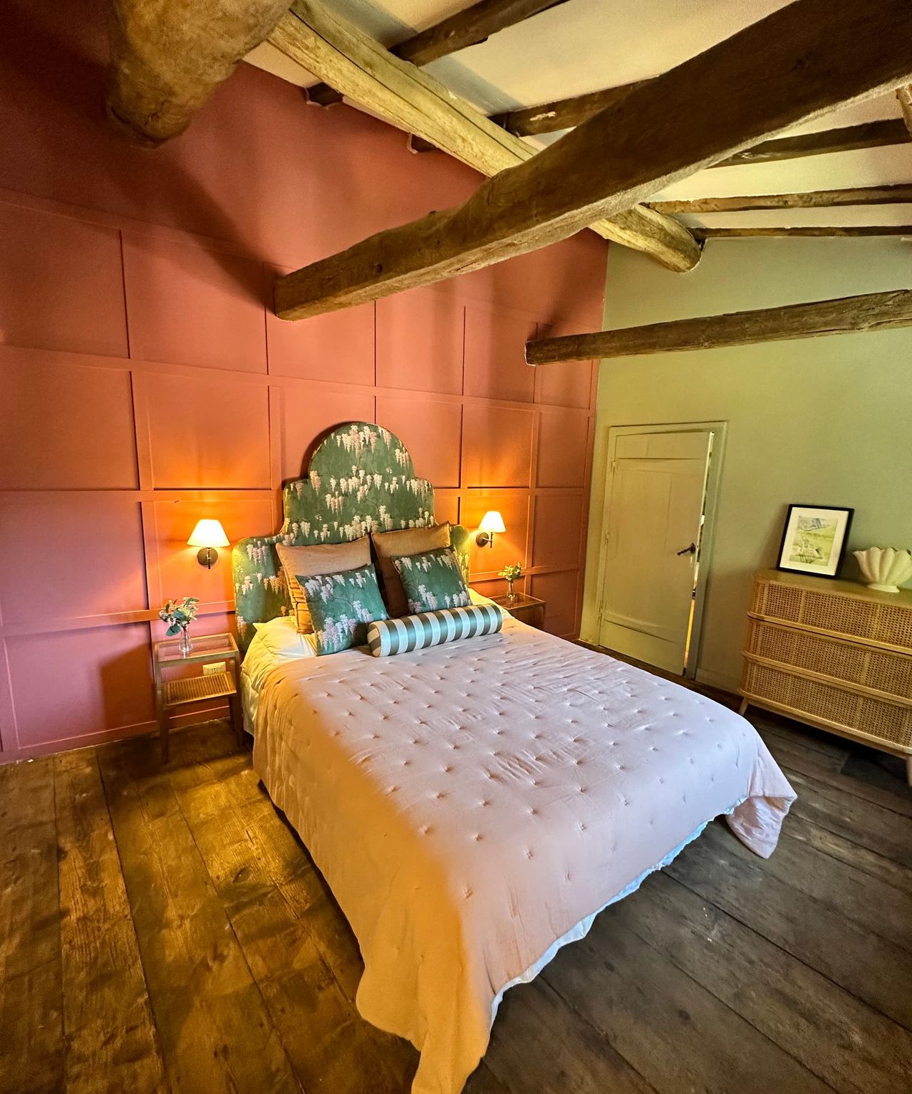 A bedroom with pink covers and wooden beams and flooring