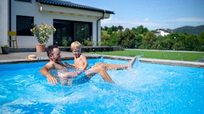 Man swimming with his young son in an outdoor pool at home