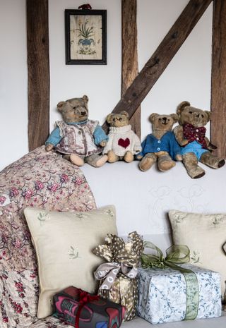 vintage teddy bears on sofa back with vintage quilt christmas presents and white walls with beams