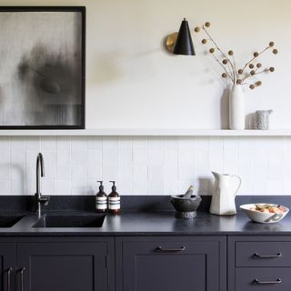 Black painted kitchen cupboards and countertop, white tiled backsplash and decorative open shelving