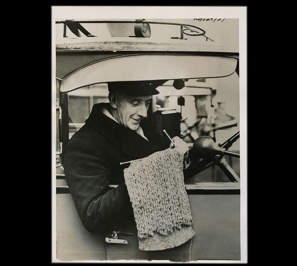 Taxicab driver knitting between fares, London, ca. 1940.