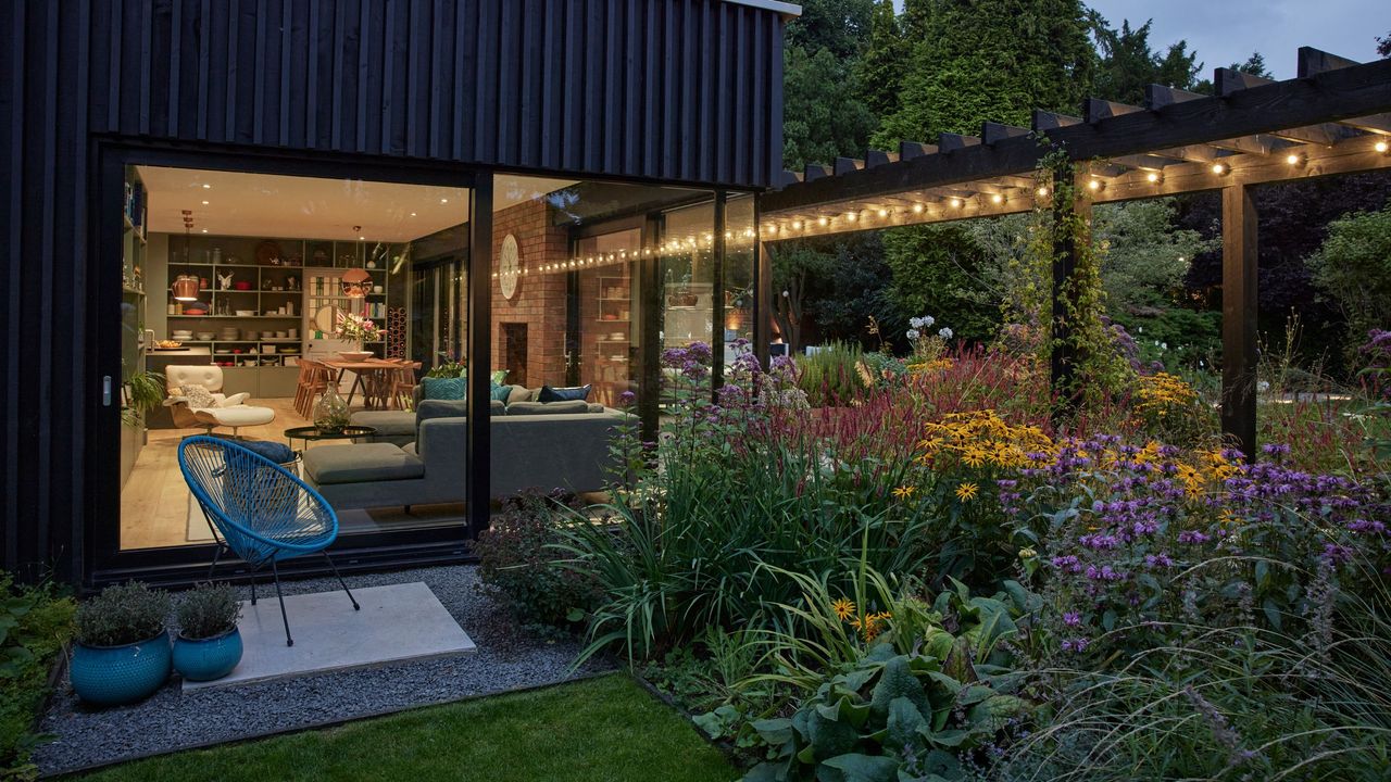 A backyard with lots of green foliage planted. Coneflowers and purple blooms are seem amidst a greenscape. 