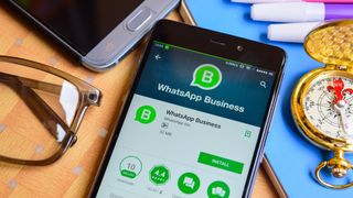 The WhatsApp Business app shown on an Android device on a desk surrounded by other items