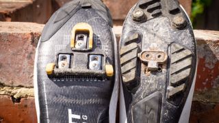 The soles of two shoes side by side, showing the two different cleats