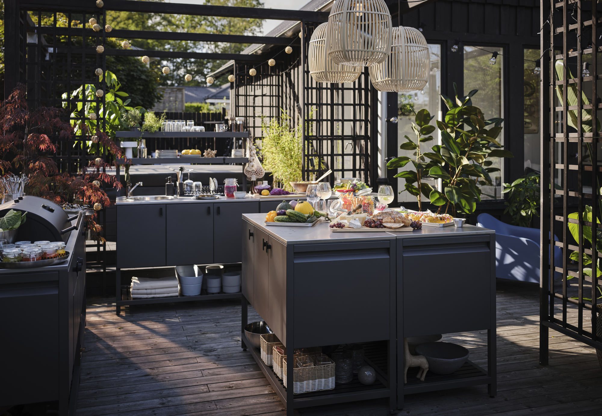 IKEA outdoor kitchen with island, bbq, storage, a sink, and lanterns overhead, with lots of food on the countertop