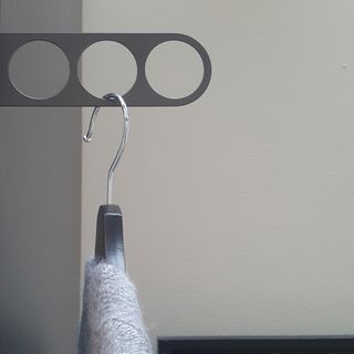 The Ikea Komplement Valet Hanger, a metal bracket attached to the side of a grey wardrobe holding a grey cardigan on a hanger