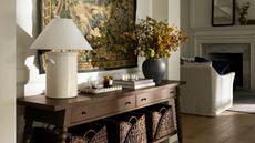 entryway table from the mcgee & co fall collection styled with a bobbin vintage style console table with a tapestry hung behind and styled with baskets, a lamp and vase with foliage