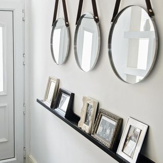a white hallway with three hanging circle mirrors and photo frames on a black shelf