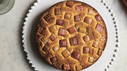 a round brown cake with chunks of rhubarb on a white platter