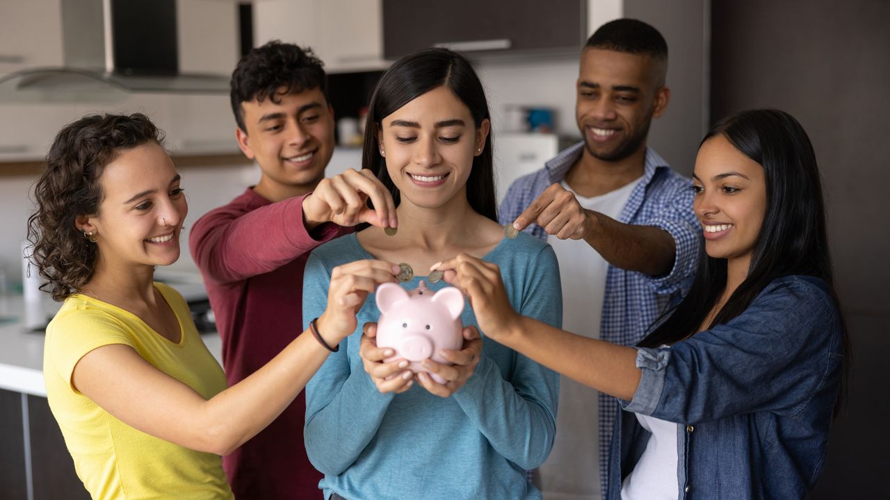 College students gather around a fellow student who&#039;s holding a piggy bank.