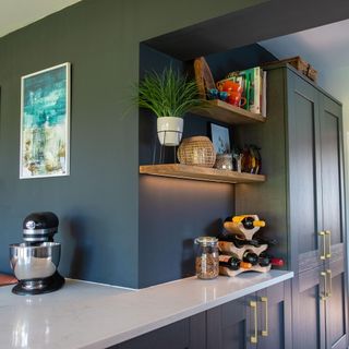 blue kitchen cabinetry and a peninsula with marble worktop and shelving above