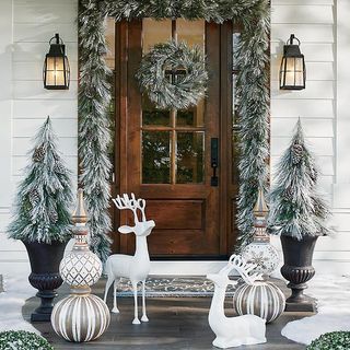Outdoor Christmas decor in a porch with snow tipped foliage and christmas trees