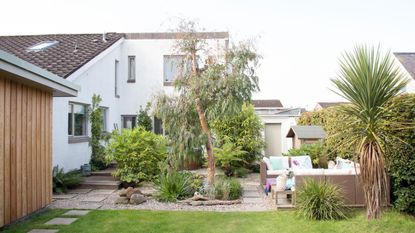 View from the lawn towards the gravelled and decked patio area with garden seating and trees. 