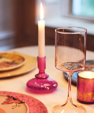 A dining table with magenta candle, candlestick holder, plates, and a tinted pink glass