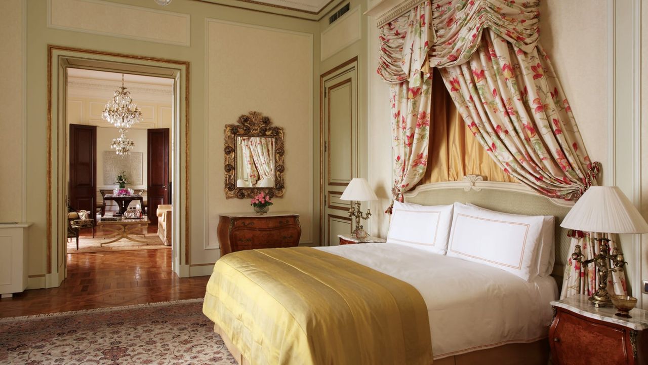 Image of a fancy bedroom in a traditional french style. The walls are light beige and light green, and the bed has a light green and pink floral canopy.