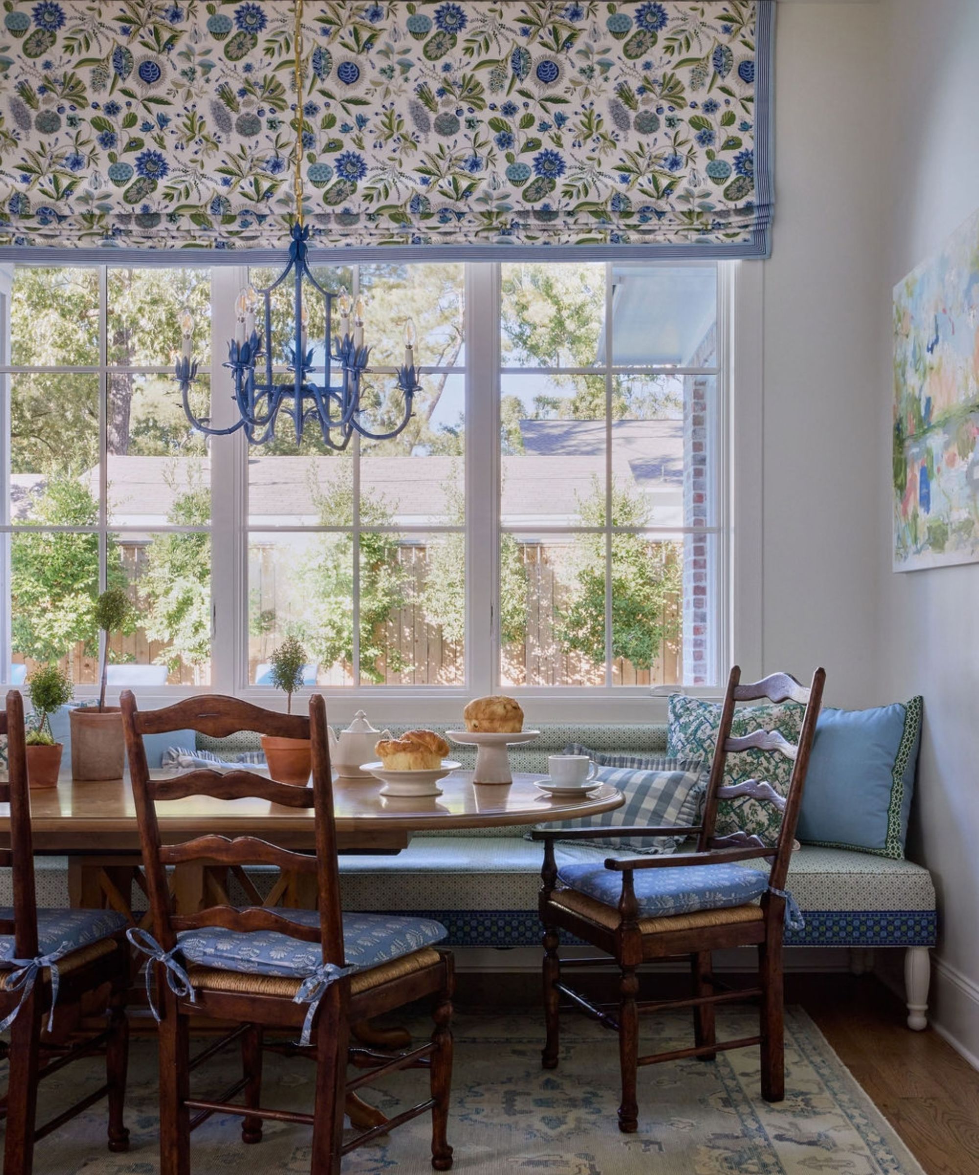 Breakfast nook with a wooden dining table, blue-cushioned ladder-back chairs, a built-in banquette, and a blue iron chandelier