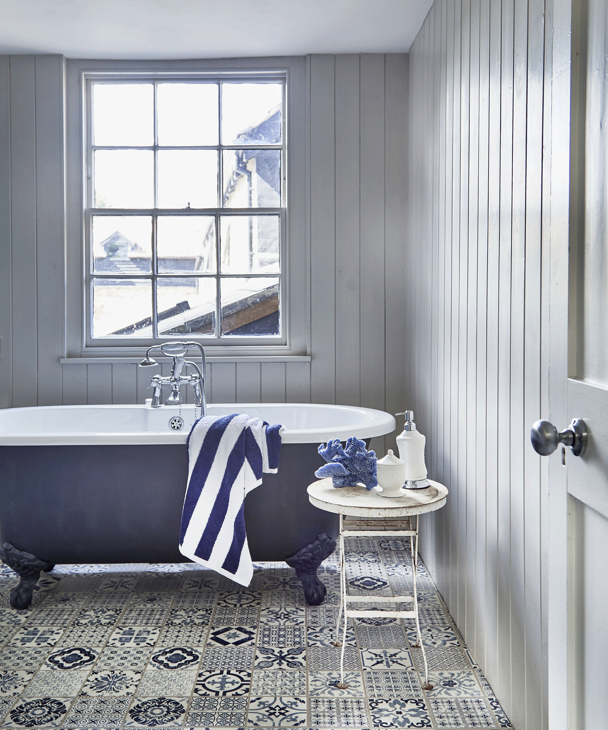 Blue and white bathroom with mosaic style luxury vinyl tiles and freestanding blue bath tub