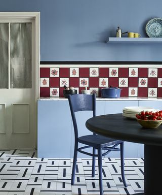 A kitchen with blue walls, dark blue painted dining set, white and blue flooring and red tiled backsplash