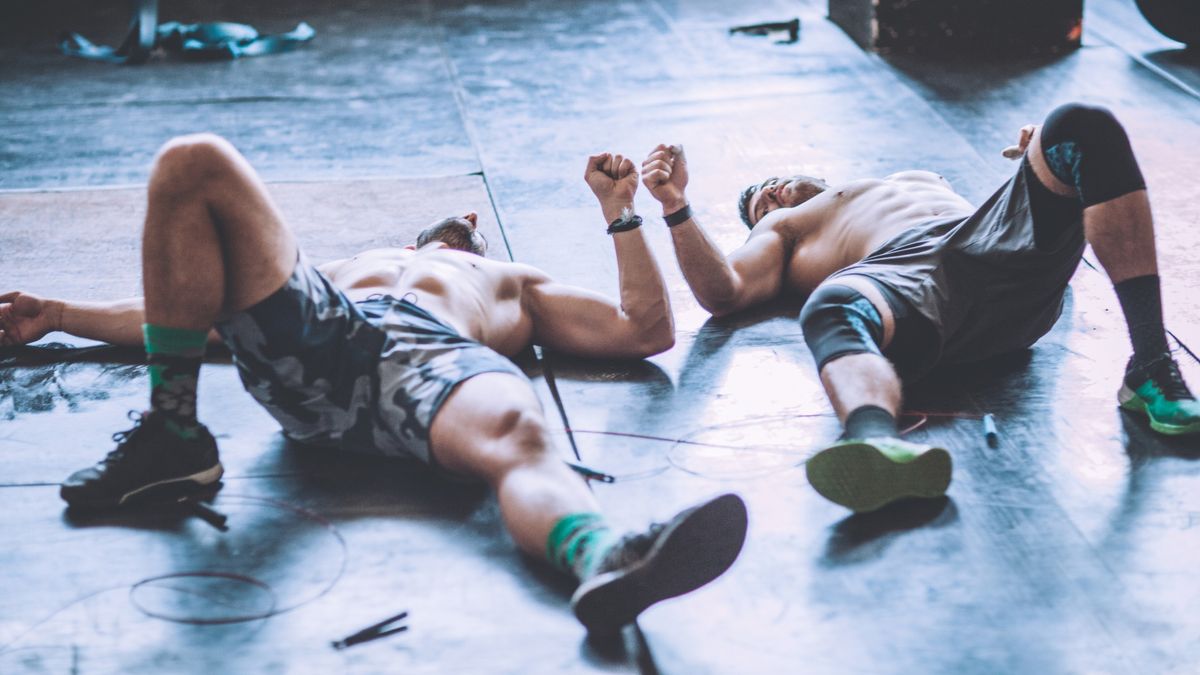 Two men lie on the gym floor, exhausted after exercise