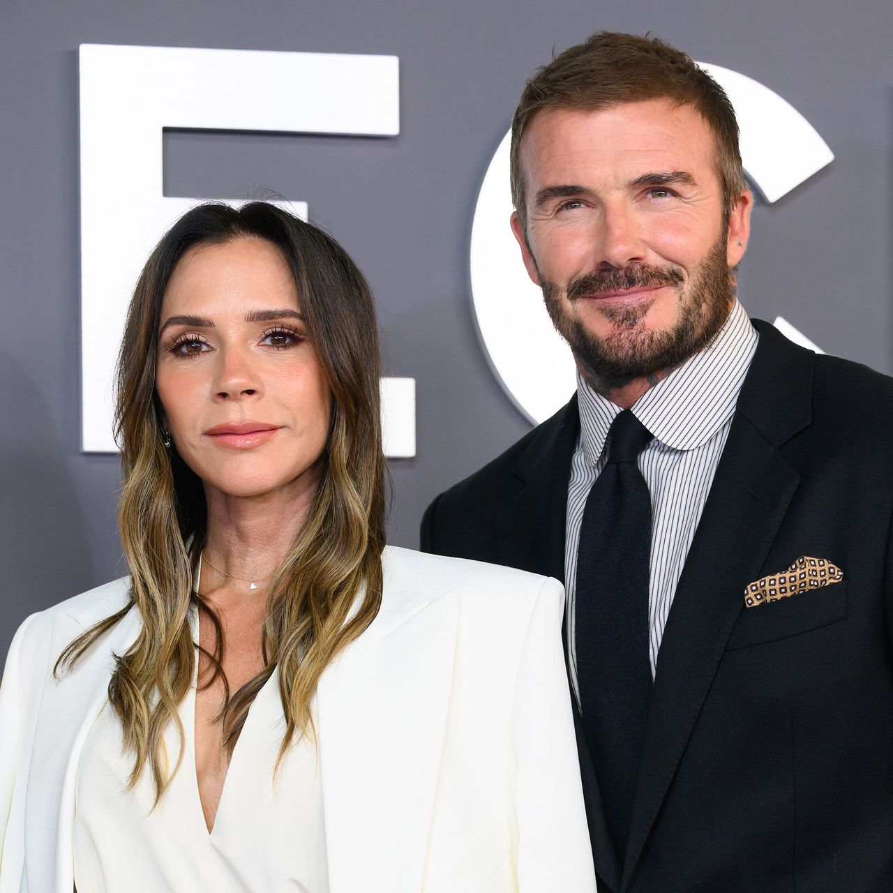 Victoria Beckham and David Beckham in front of a grey background with white lettering. The couple is attending the &quot;Victoria Beckham&quot; World Premiere.