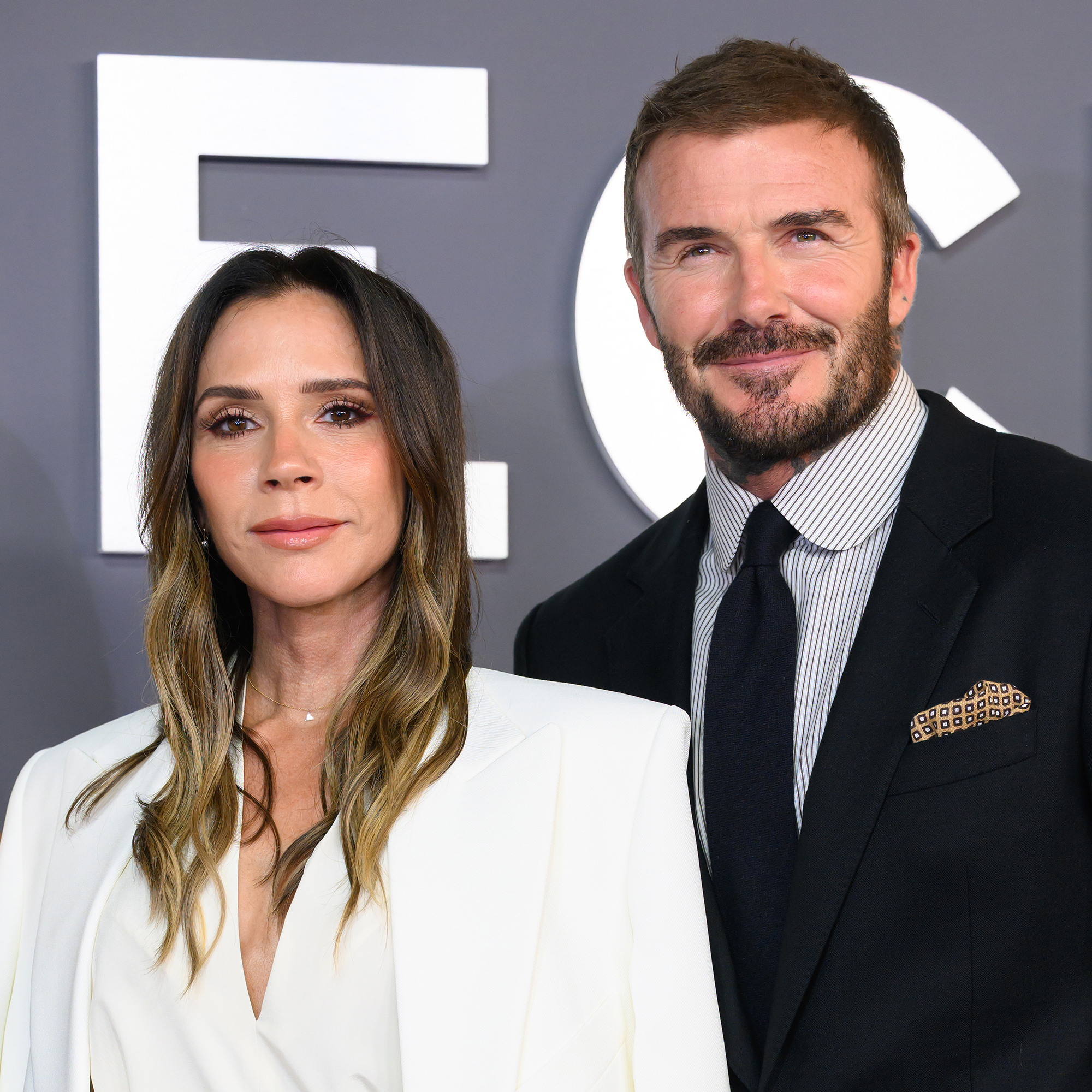 Victoria Beckham and David Beckham in front of a grey background with white lettering. The couple is attending the &quot;Victoria Beckham&quot; World Premiere.