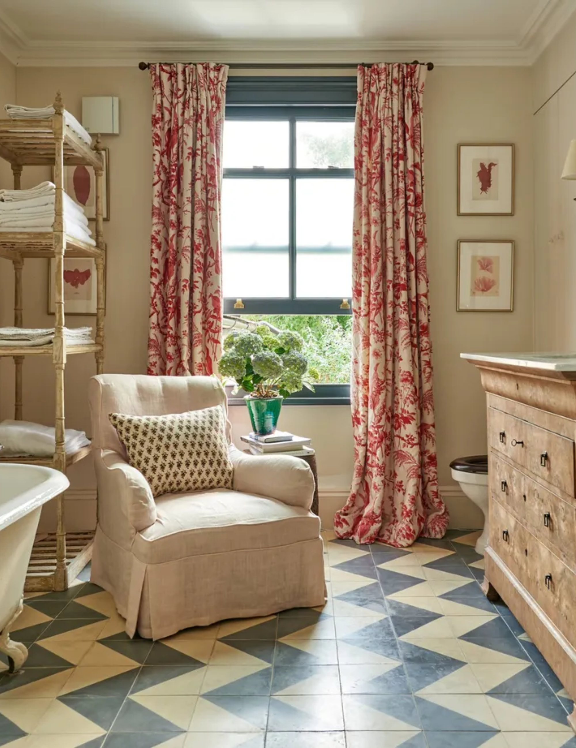Traditional bathroom with chintzy floral drapes, vintage wood furniture, chevron tiled floor and an armchair