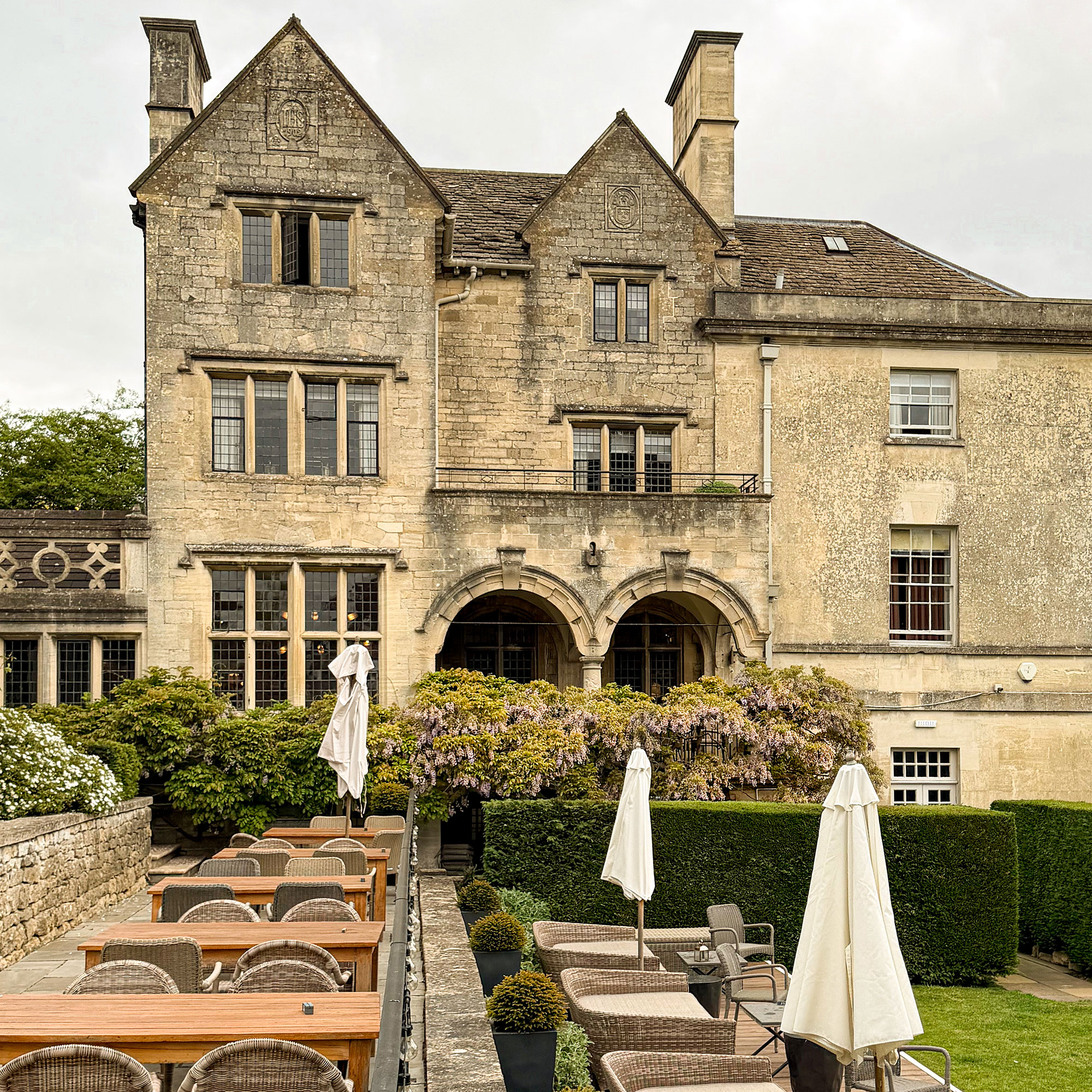 Exterior of traditional English stone manor house with row of wooden tables and rattan chairs on patio