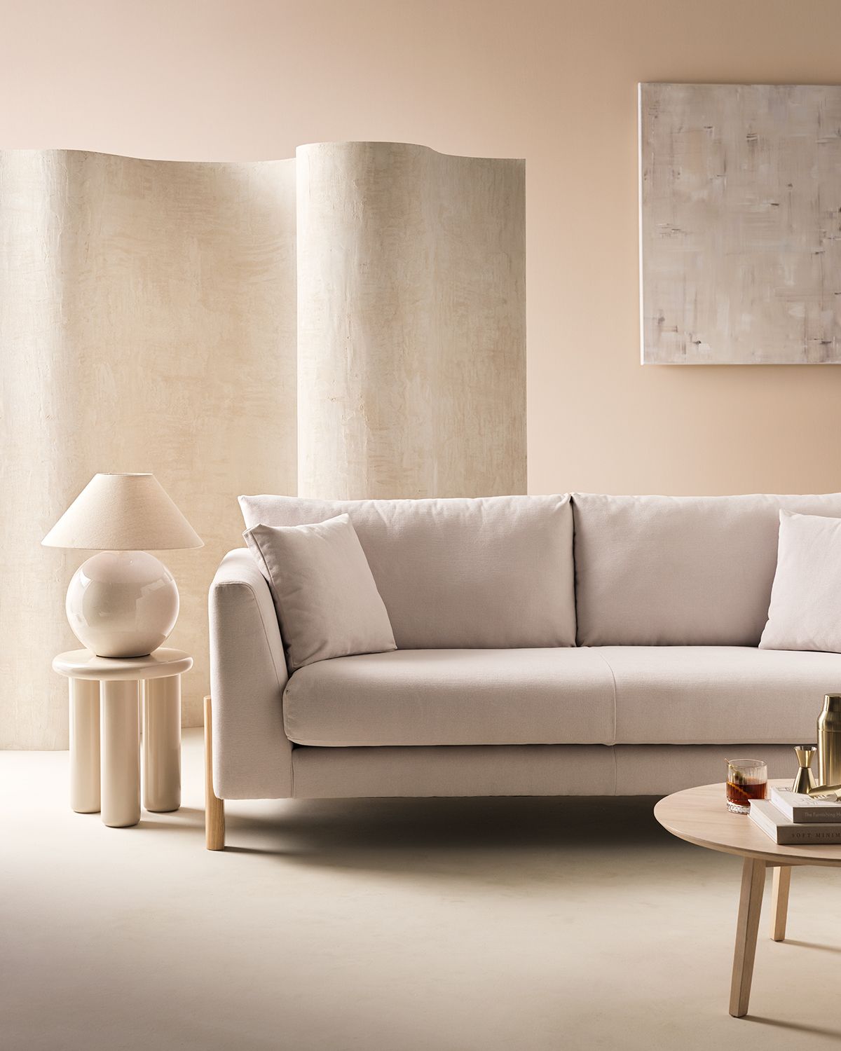 Image of a room drenched in an off-white color. There is an off-white room divider and a light gray/off-white sofa. Beside the sofa is a high-gloss side table with a matching sphere table lamp.