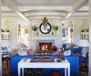 beamed living room with fire lit, blue sofas red and blue patterned cushions and boat pictures