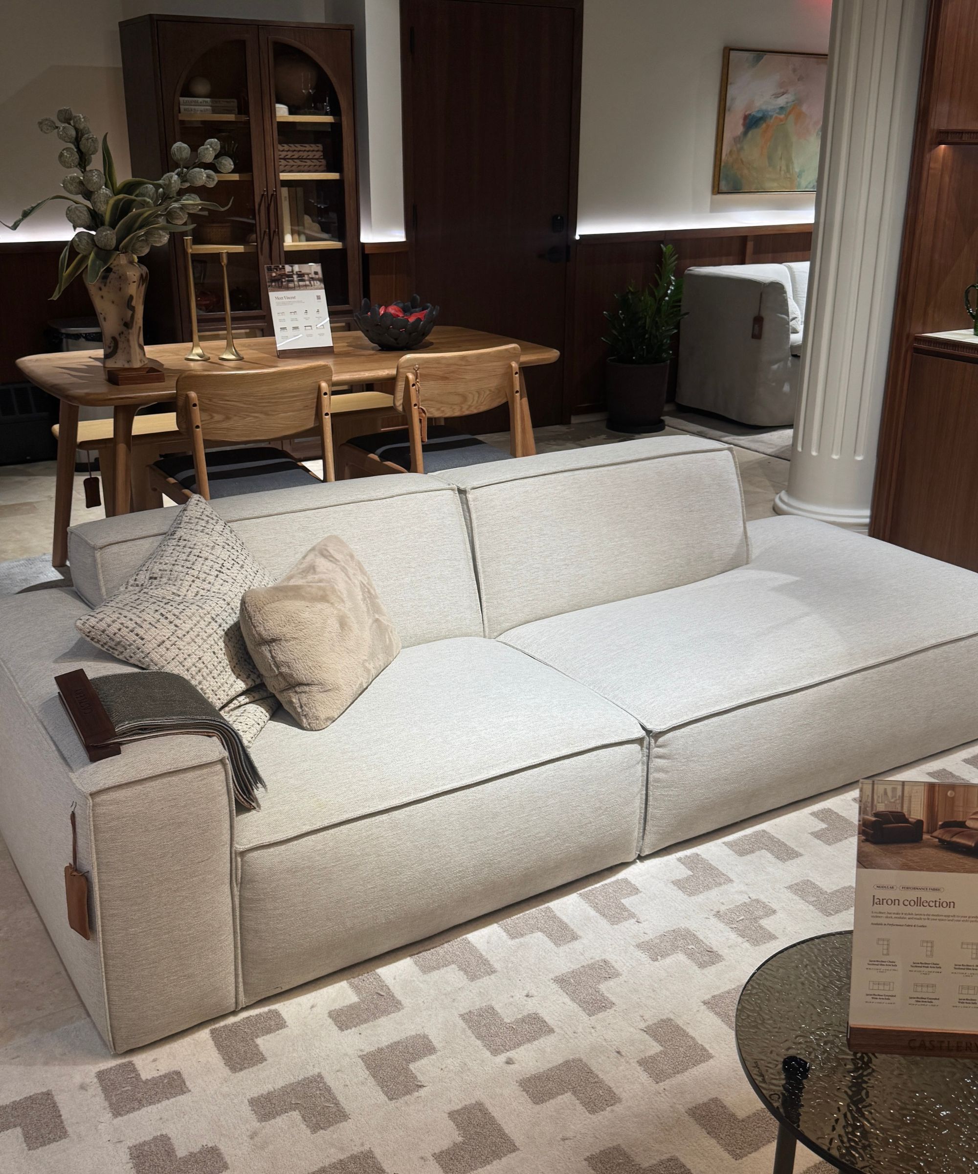 white sofa with clean lines and arm on one side, with dining table in the background, checked gray and white rug, and glass coffee table