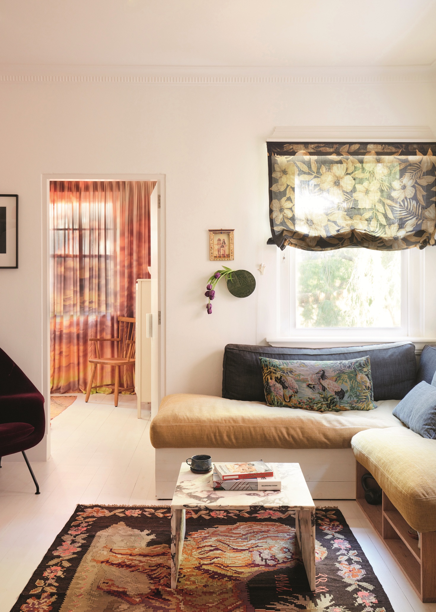 living room with sheer floral roman blinds, a banquette seat with patterned rug, stone coffee table and white floors and walls