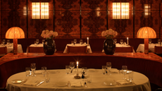 curved booth table with white tablecloths in a burl-wood clad restaurant. The space is low-lit and feels cozy and warm, yet glamorous
