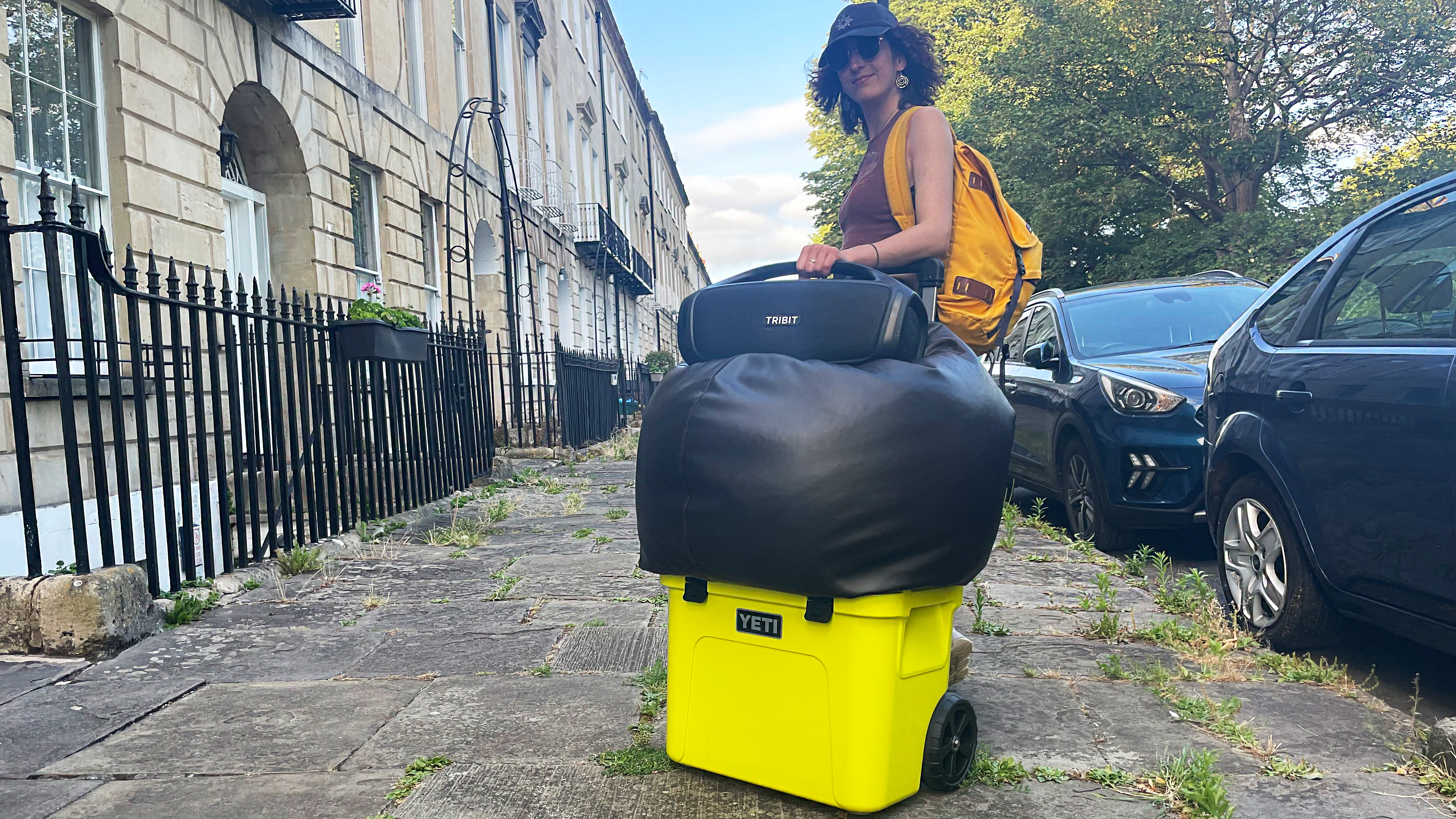 the author with the yeti roadie wheeled cooler, a speaker, and a bean bag, on the pavement next to a road