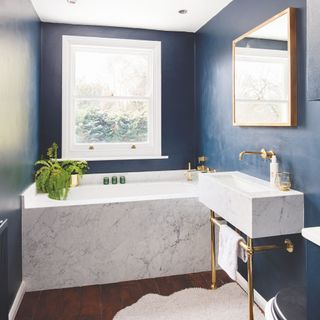 Blue painted bathroom with marble bath and sink with brass hardware