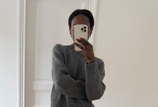 Woman wearing grey cashmere sweater and black pencil skirt, taking mirror selfie.