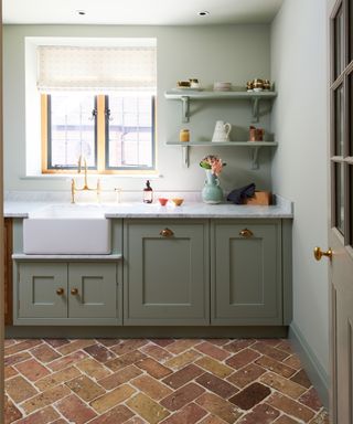 green fitted kitchen area with brick paver flooring