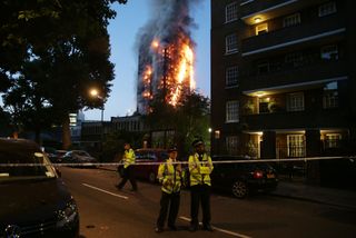TOPSHOT - Police man a security cordon as a huge fire engulfs the Grenfell Tower early June 14, 2017 in west London. The massive fire ripped through the 27-storey apartment block in west Lond