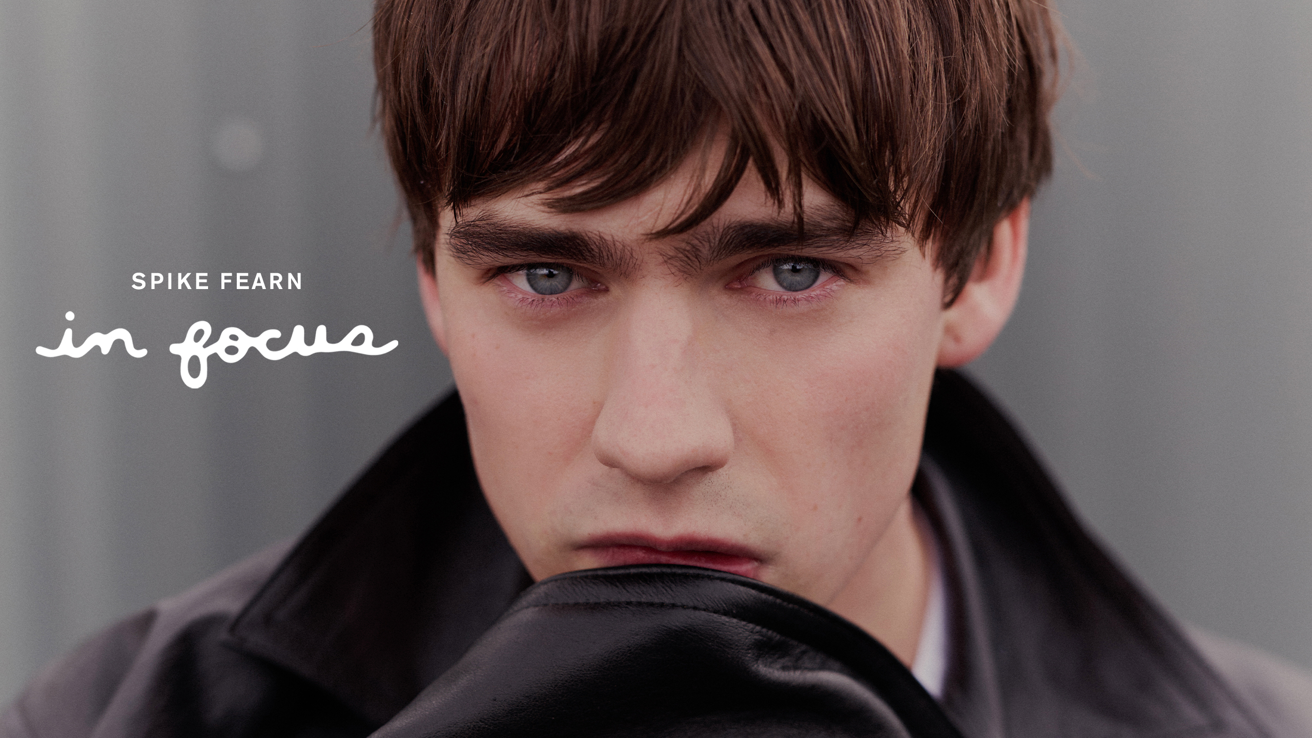 Actor Spike Fearn for Who What Wear&#039;s December In Focus story. This close-up shot of the actor shows his looking to camera wearing a leather Prada jacket with the sleeve up to his mouth. 