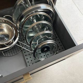 Interior of a pan drawer with pan lids organised using a plastic peg board