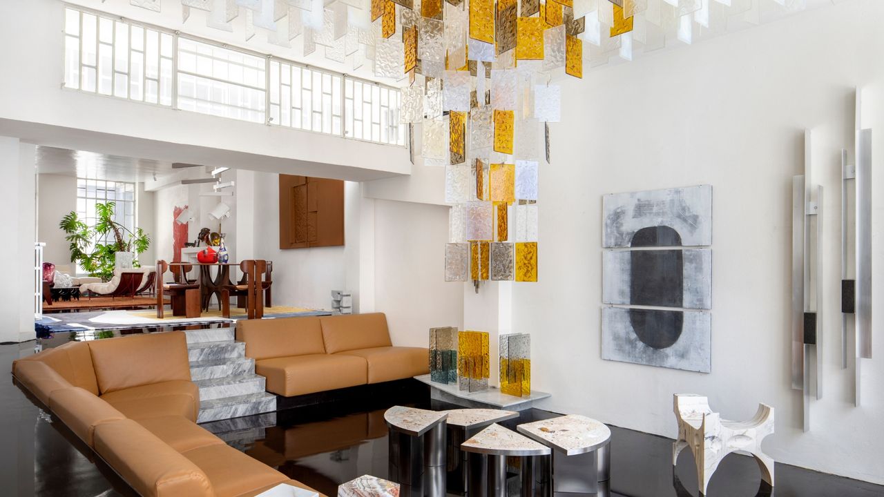 A modern living room featuring a mixture of mid-century modern and contemporary glamour decor showcases a stunning golden and white Murano glass chandelier along with leather furniture, sleek coffee tables, and wall art.