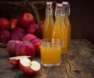 A glass of apple juice on a dark wood board, surrounded by red apples.