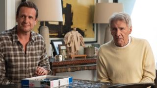 From left to right: Jason Segel as Jimmy sitting at a table with a puzzle on it next to Harrison Ford as Paul. 