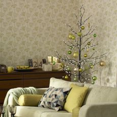 A living room with a botanical wallpaper decorated for Christmas with a twig Christmas tree decorated with green baubles