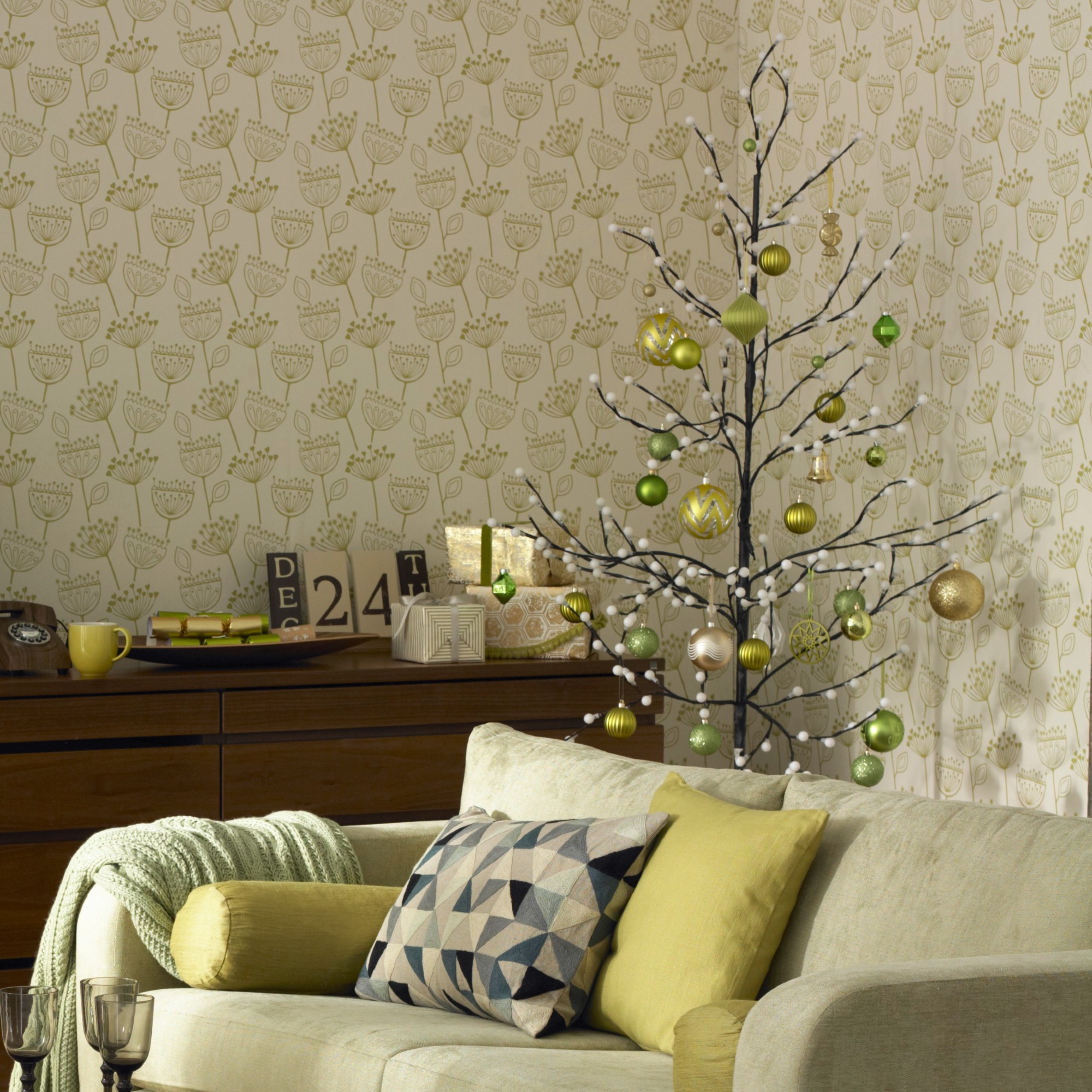 A living room with a botanical wallpaper decorated for Christmas with a twig Christmas tree decorated with green baubles